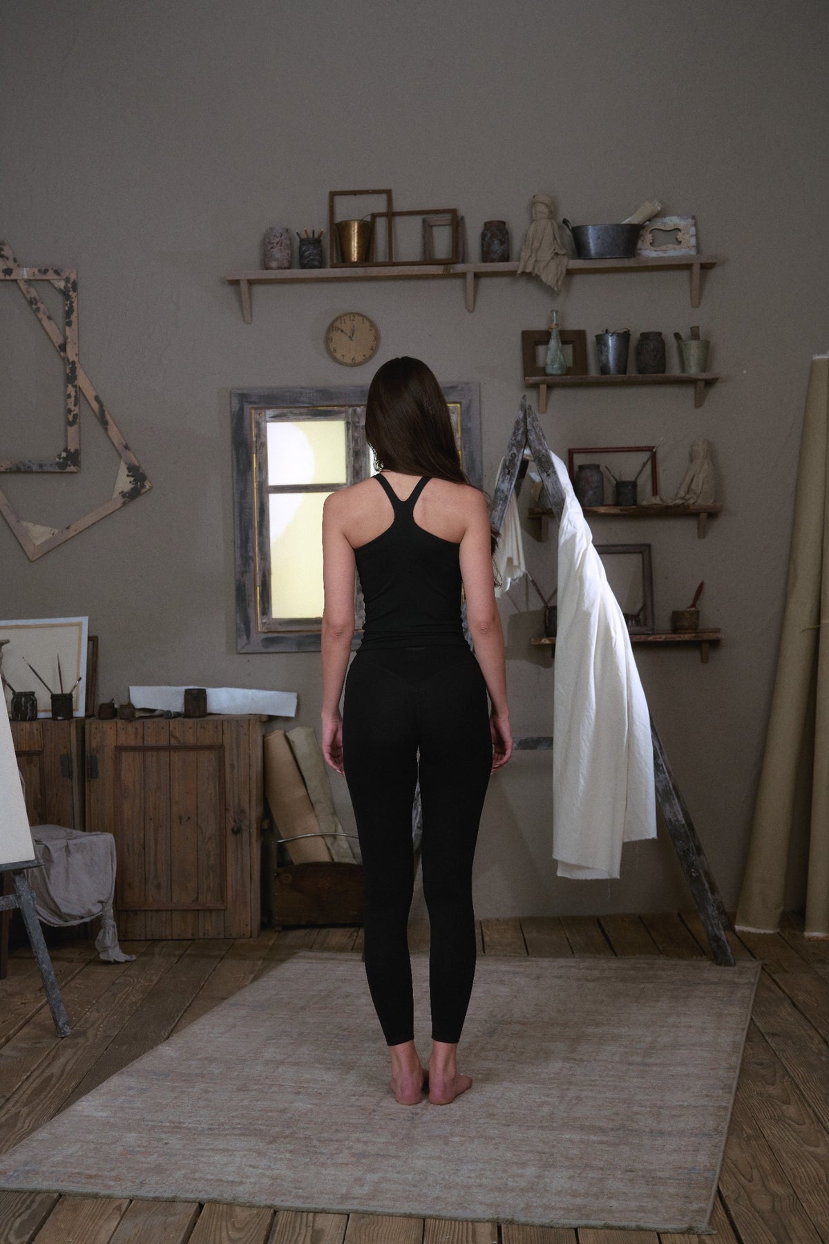 Woman shown from behind wearing amphr black high-waisted leggings and racerback tank top, full-length studio shot
