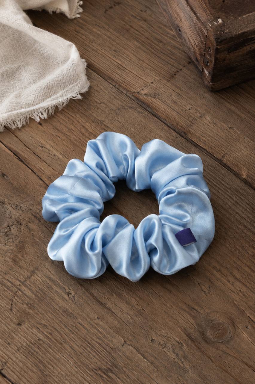 amphr light blue satin scrunchie with branded tag on a wooden surface